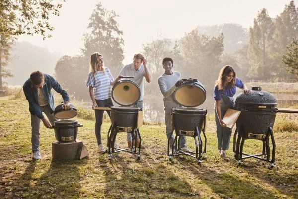 Patru kamado-uri Grill Guru Original de dimensiuni diferite, afara in natura, cu persoane langa ele.